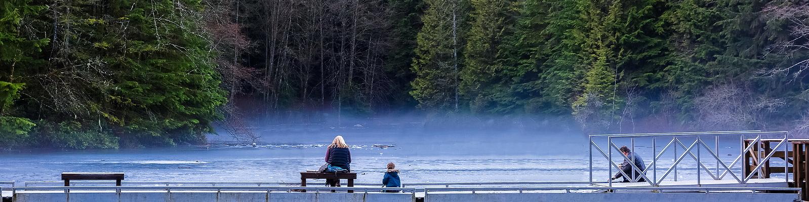 A family sitting in front of a misty lake in Lynn Canyon Park