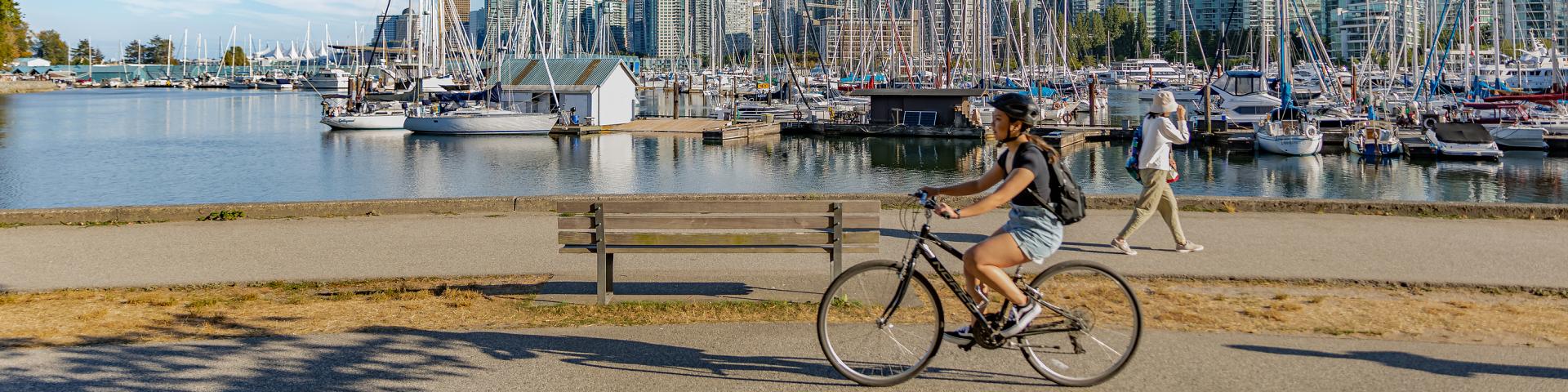 Vancouver, British Columbia, Canada in summer day. Unidentified tourists and bicyclists at Stanley Park and Vancouver Skyline with marina