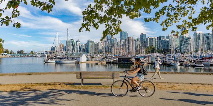 Vancouver, British Columbia, Canada in summer day. Unidentified tourists and bicyclists at Stanley Park and Vancouver Skyline with marina