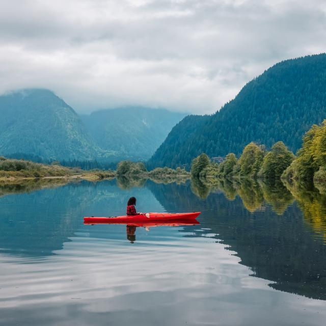 Photo of kayaker surrounded by water and beautiful mountains and trees during a fall day in Vancouver.