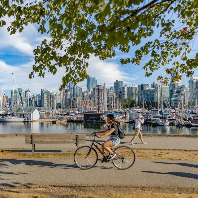 Vancouver, British Columbia, Canada in summer day. Unidentified tourists and bicyclists at Stanley Park and Vancouver Skyline with marina